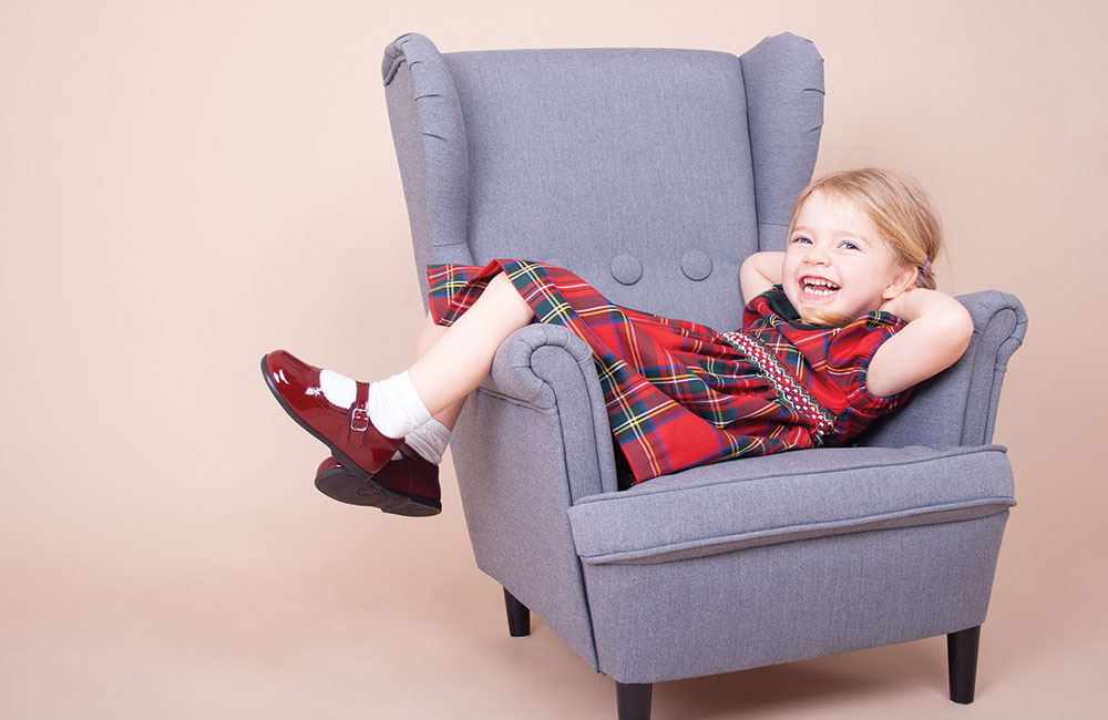 Young girl lain in a big chair wearing a tartan dress and Early Days shoes