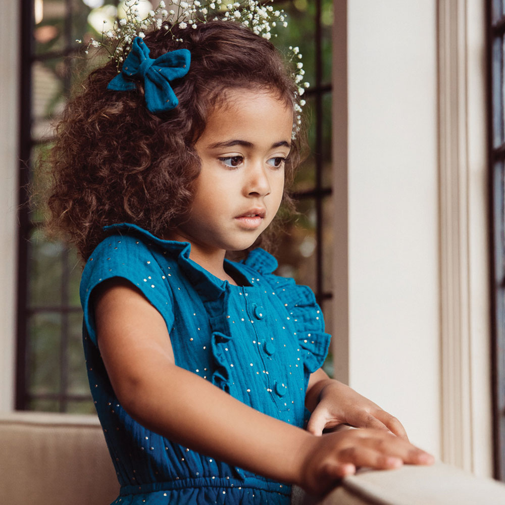 Young girl in blue dress looking out through a window