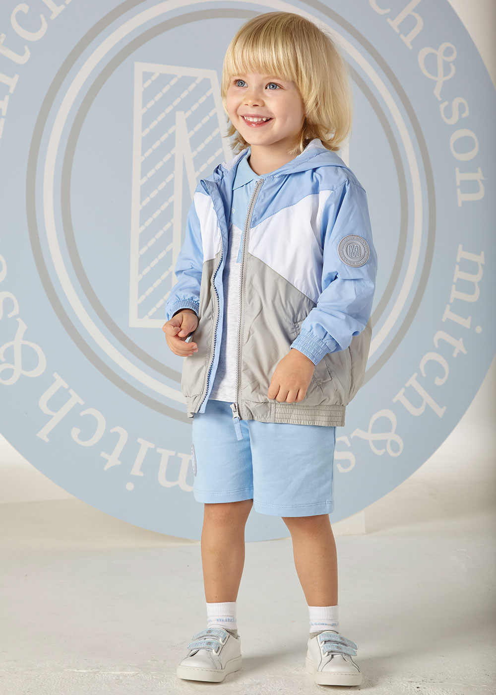 Blonde haired boy in pale blue jacket and shorts