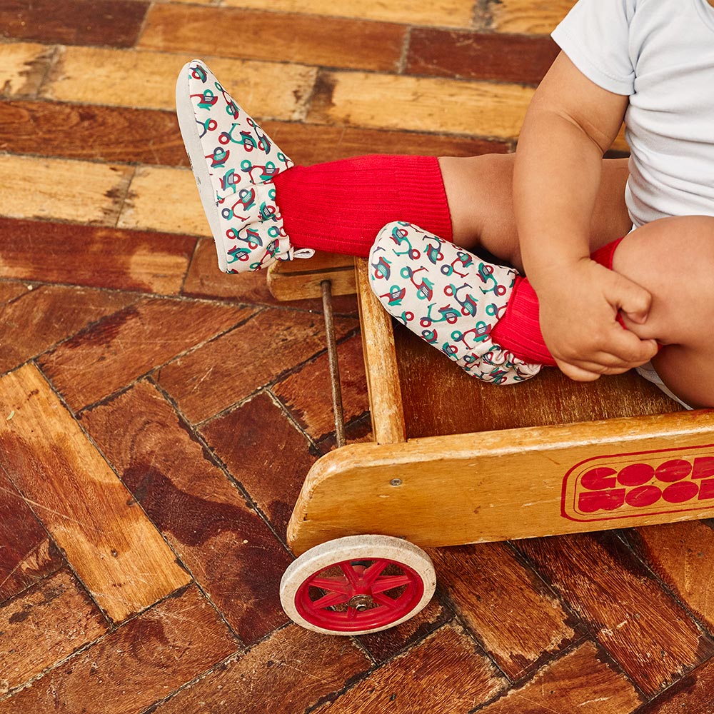 Baby sat in wooden trolley wearing Poco Nido baby shoes