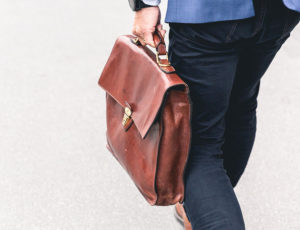 Business man in jeans and blue jacket walking and holding a brown briefcase