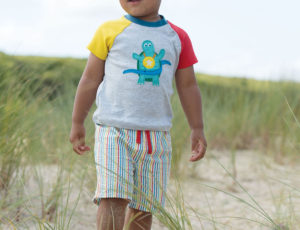 Young boy at the beach in Colourful Frugi shorts and T Shirt
