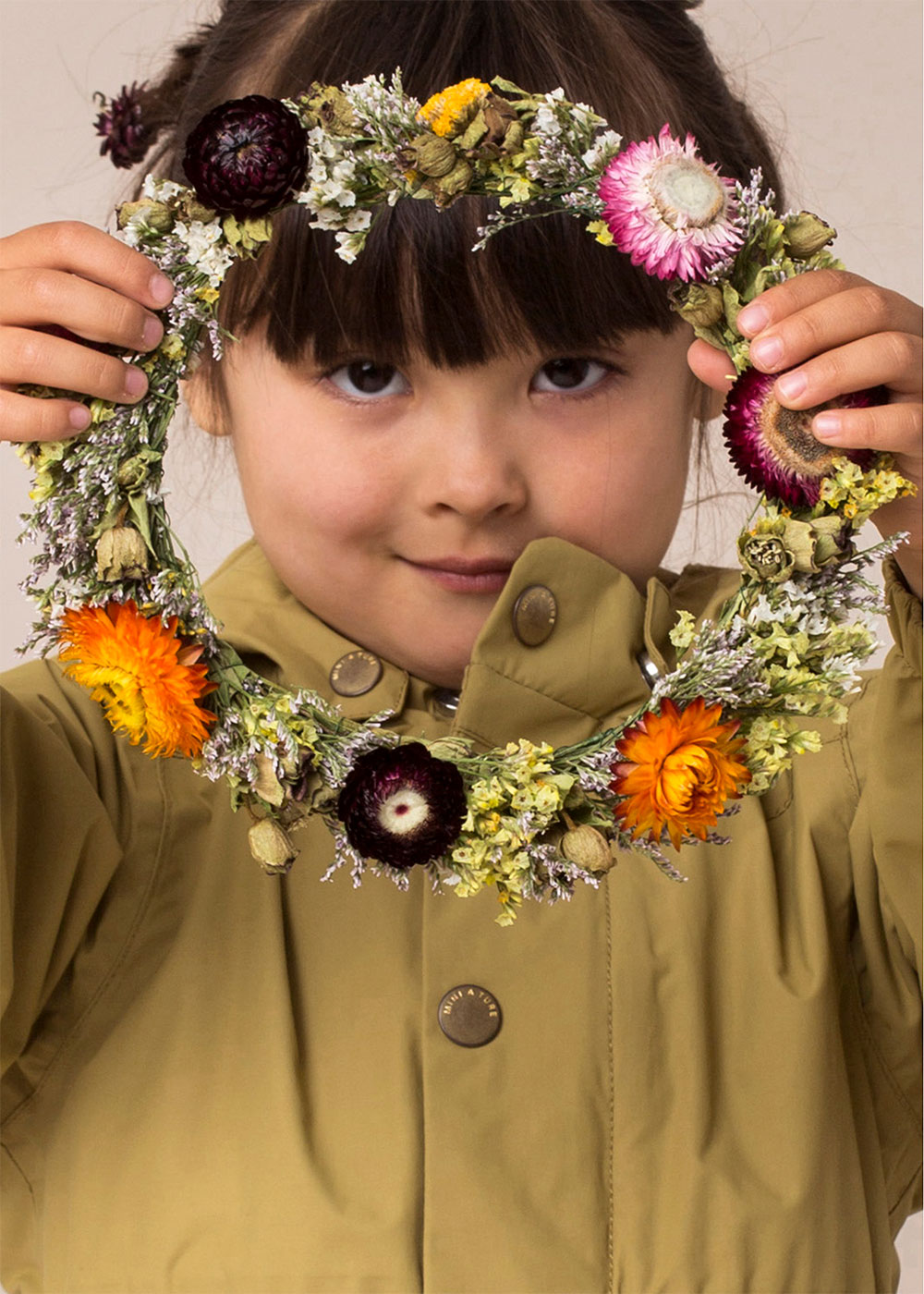 Young girl in green Mini A Ture coat holding a ring of flowers
