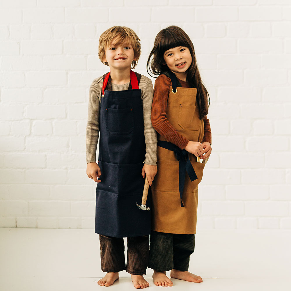 Two young children stood against a white wall