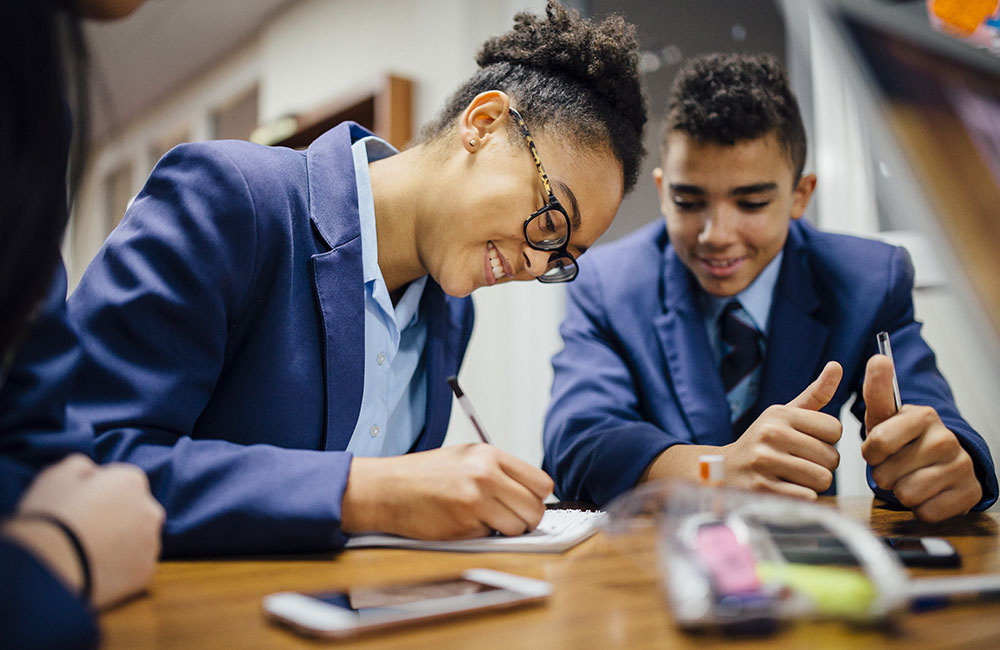 Two school pupils sat writing. FTCT school uniform grants.