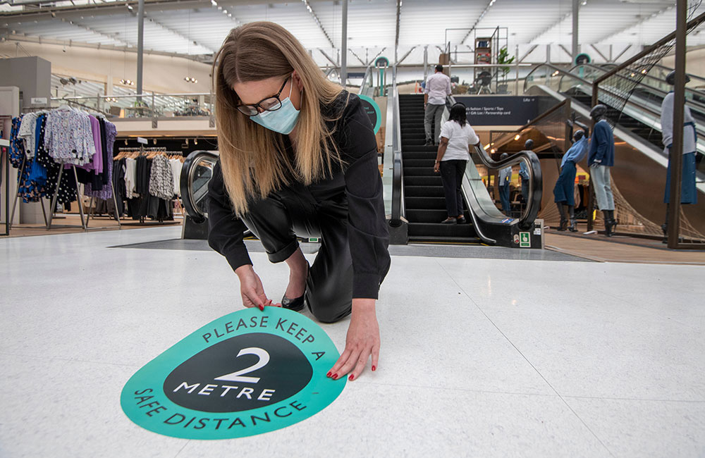 A member of John Lewis staff placing social distancing signage in store in preparation to reopen