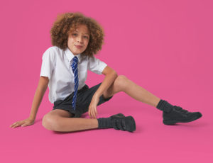 Schoolboy with curly hair against a pink background