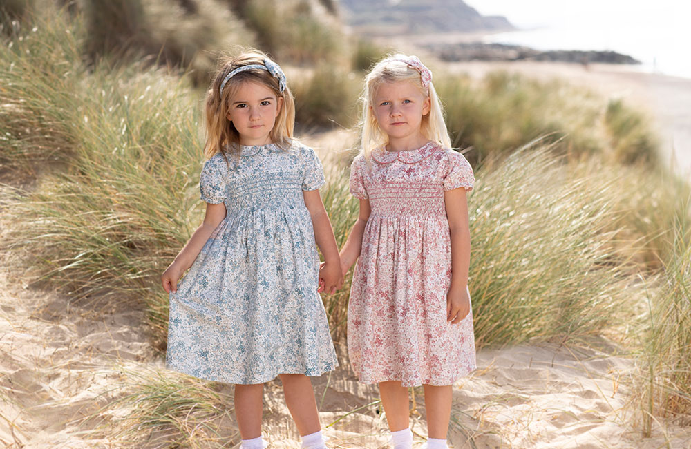 Two young girls and floral Trotters dresses holding hands on the beach