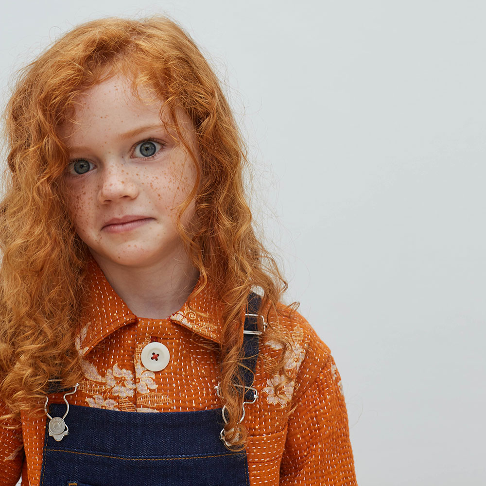 Young girl with ginger hair, wearing orange knit Chapter jumper and blue dungarees