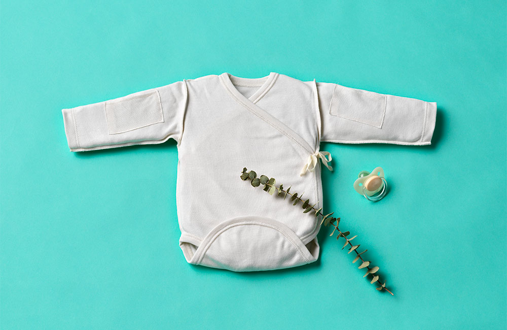 Pale grey childs babygro spread out on green background