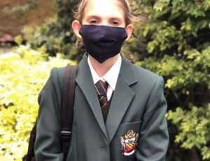 School girl in green blazer wearing a black face covering