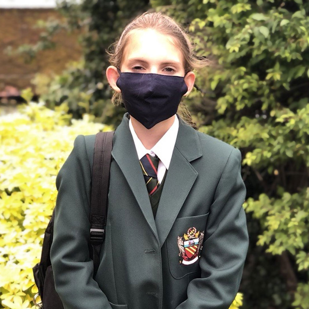 School girl in green blazer wearing a black face covering