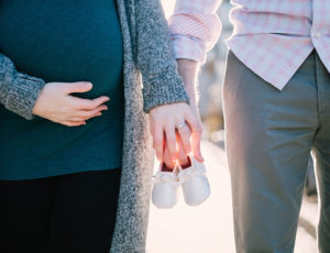 couple holding hands and a pair of white baby shoes