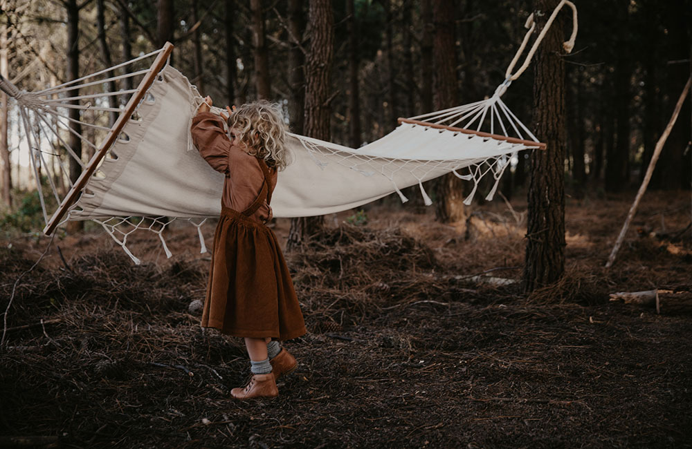 Young girl dress in brown playing with a hammock in the woods