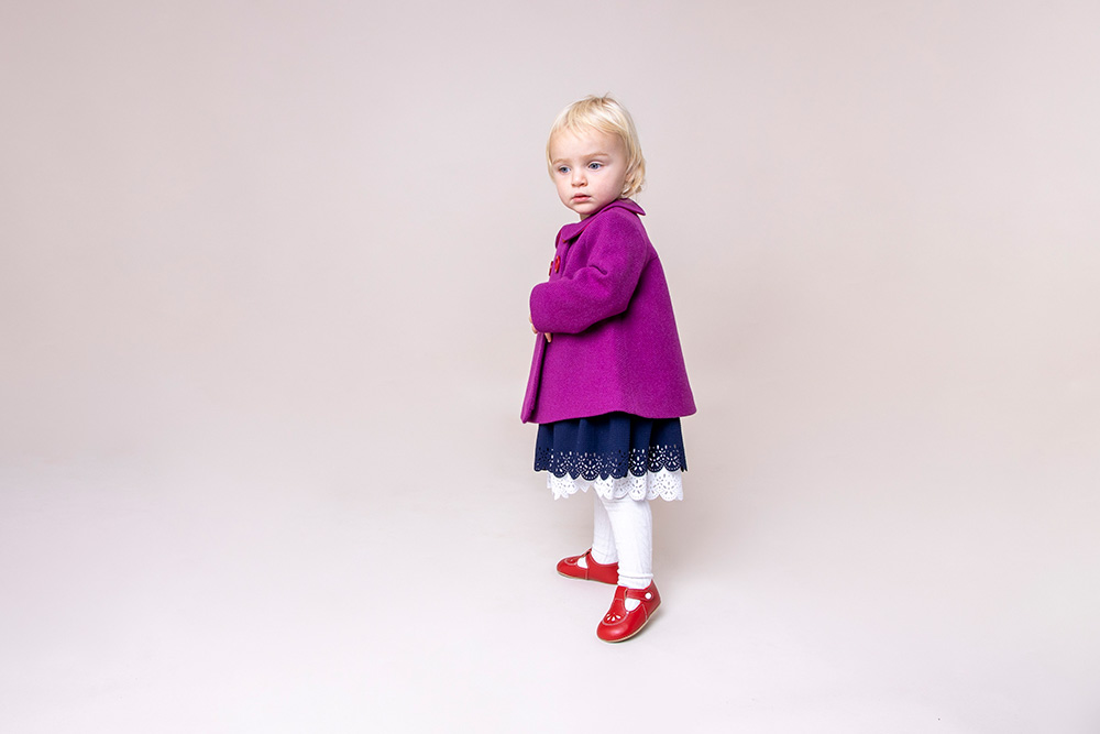A young girl stood up wearing a purple jacket and pre-walker baby shoes