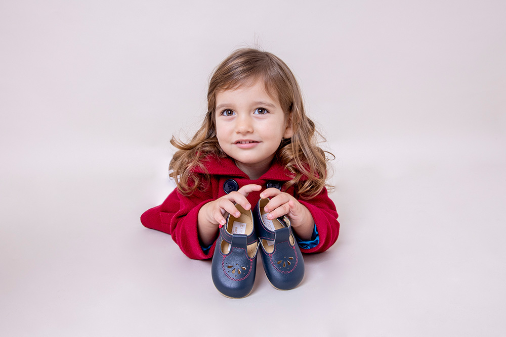 A young girl wearing a red jacket laid on the floor holding a pair of shoes