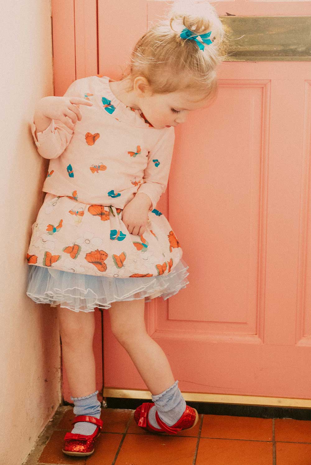 A young girl stood in the kitchen wearing a dress with butterflies on it.