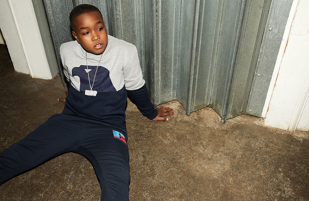 Young boy sat on floor, wearing tracksuit and sweater with Eagle motif