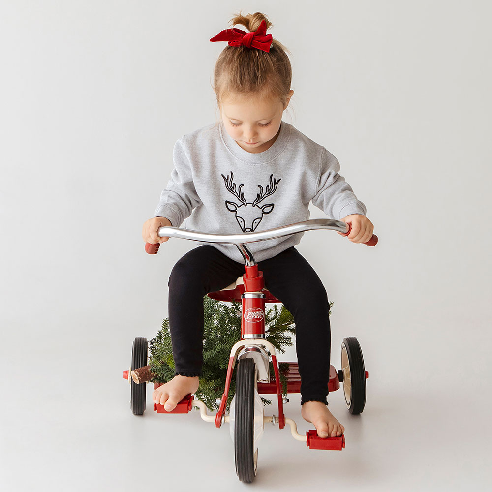 Young girl on red tricycle in grey jumper with gold reindeer motif