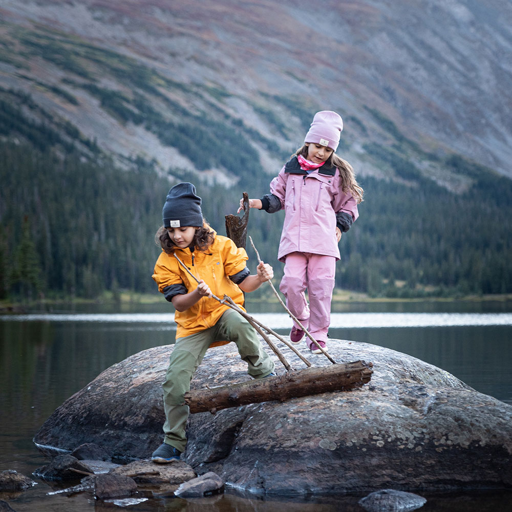 2 children playing on a rock on the edge of a lake