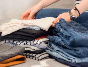 Woman sat of floor neatly folding a pile of clothes