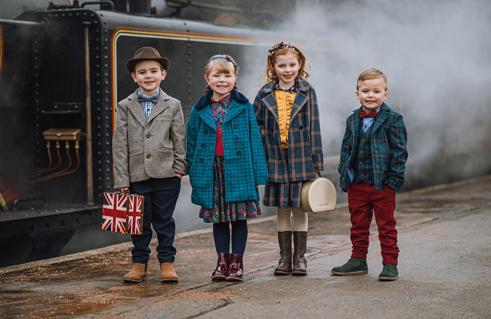 Four children stood on railway platform with steam train