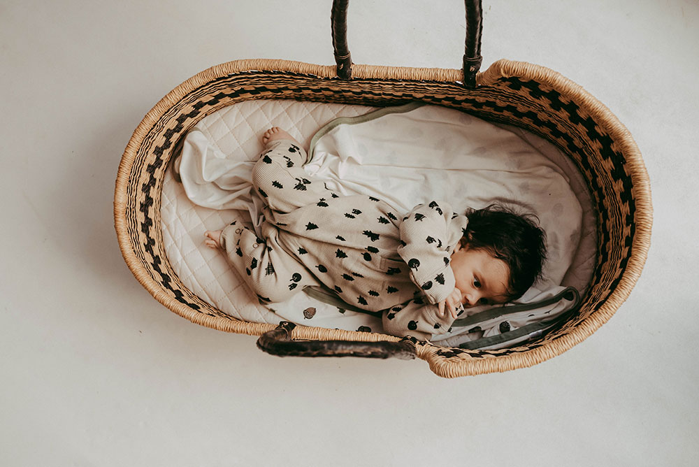 A young baby in a Moses basket wearing a grey baby grow