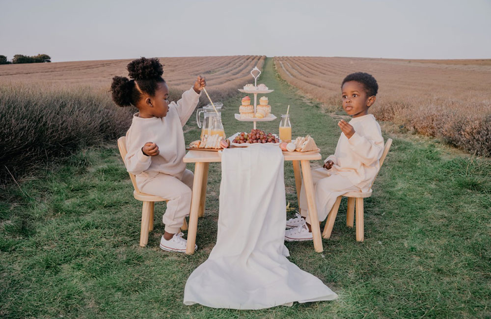 Two children sat at a table in a field - To Be Young childrenswear brand