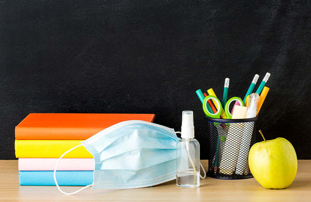 Education image of school books, pens and apple along with facemask - Education Recovery Commissioner