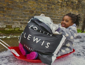 A young girl sat on a sledge holding a bag of clothing donated from John Lewis