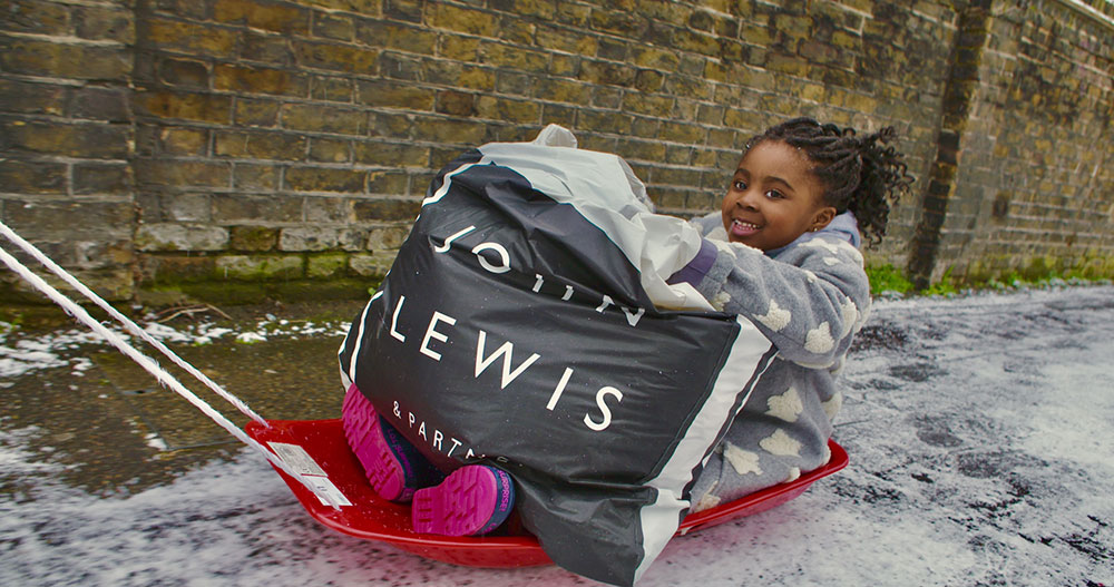 A young girl sat on a sledge holding a bag of clothing donated from John Lewis