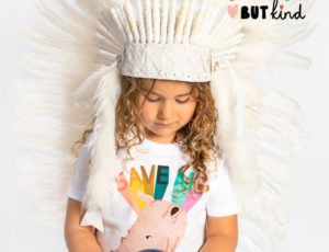 Girl with blonde curly hair wearing white indian headdress