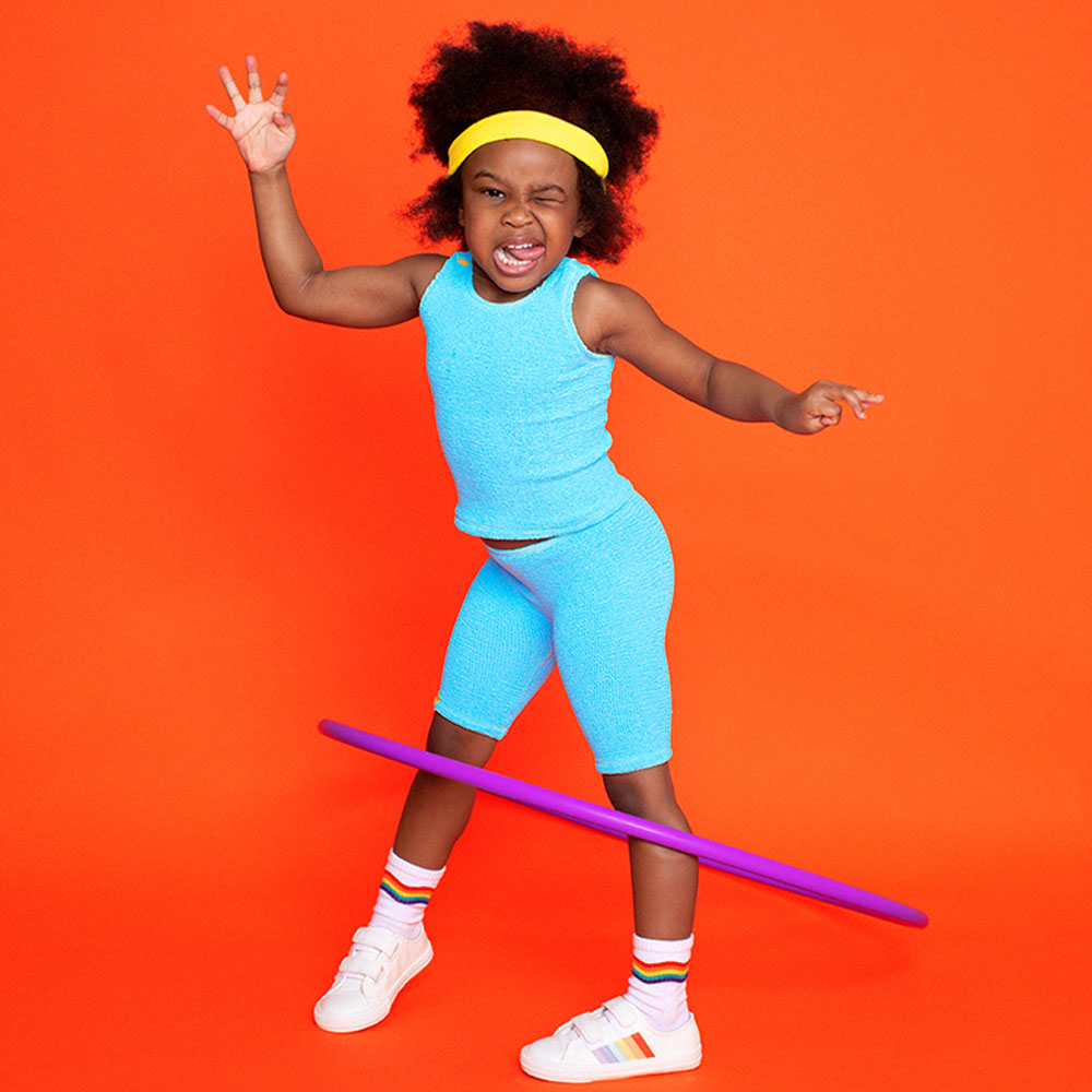 young boy in pale blue mini maxx activewear against a bright orange background