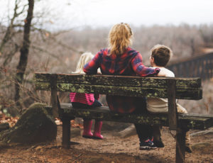 Parent sat on a wooden bech with her 2 young children