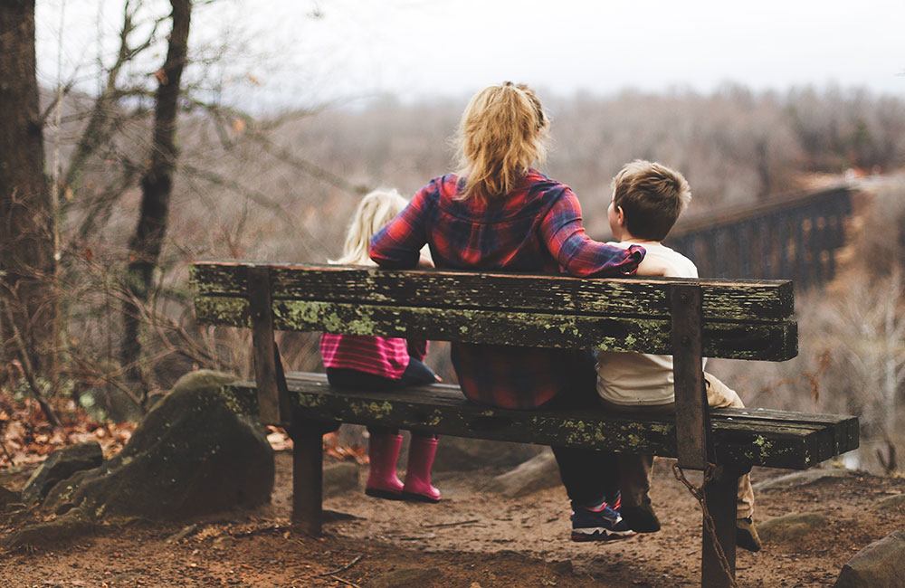 Parent sat on a wooden bech with her 2 young children