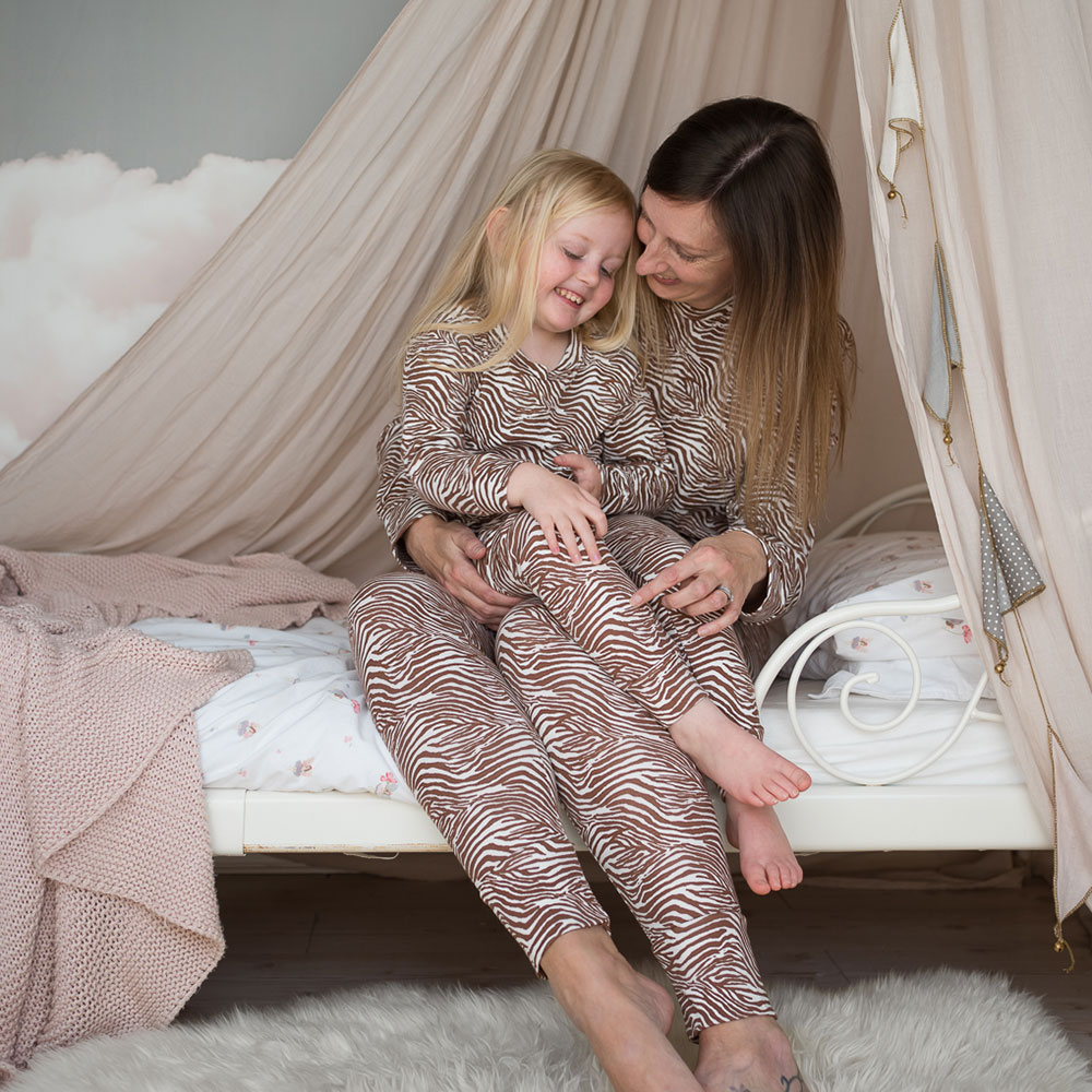Mum and daughter sat on bed in matching beige Twinkledust pyjamas