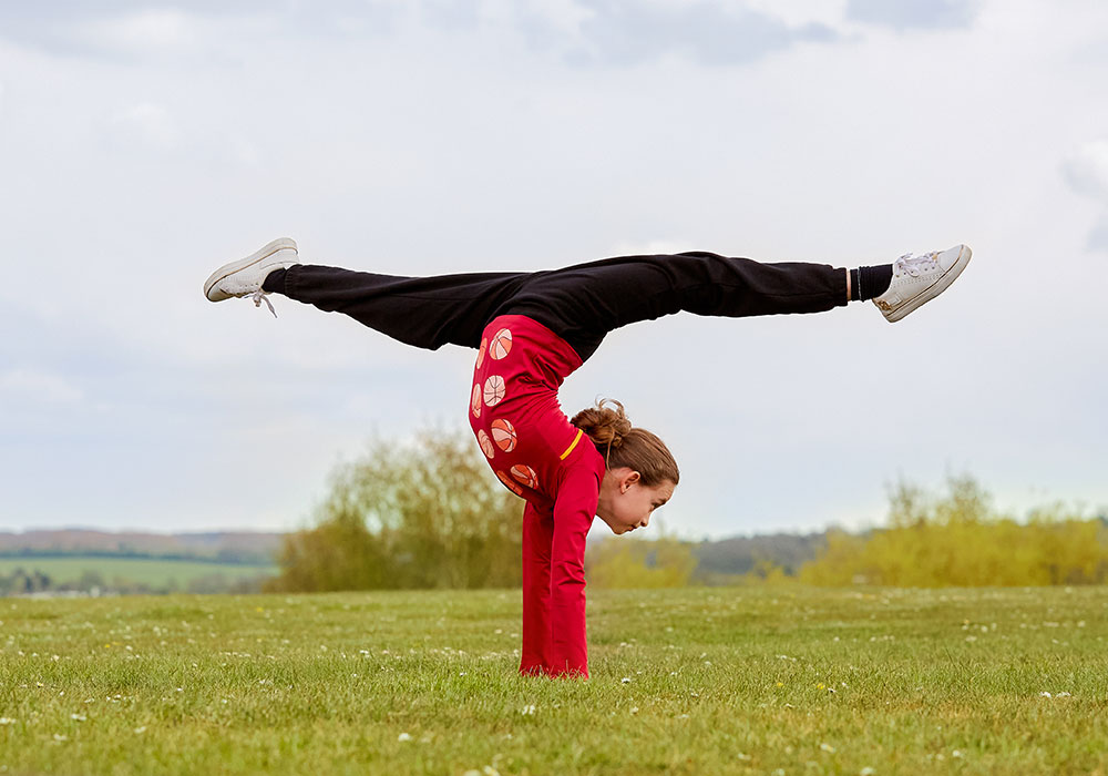 Young girl in red top and black Beech sports trousers doing a handstand