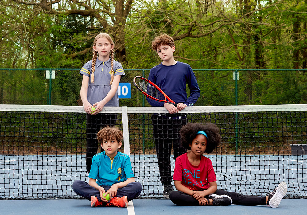 Four children sat on a tennis court wearing Beech Kids Sportswear