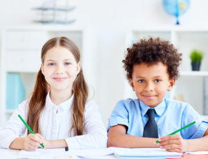 Girl and boy sat at a desk both wearing school uniform