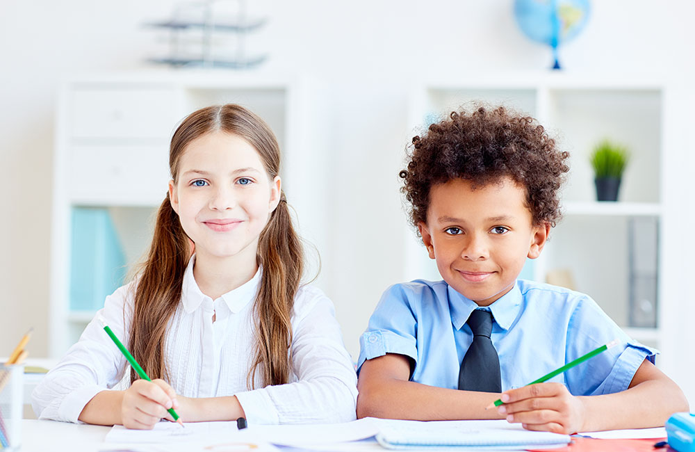 Girl and boy sat at a desk both wearing school uniform