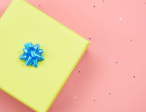 Yellow gift box with blue bow on top of a pink background