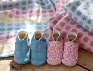 Pair of pink and blue Inch Blue toddlers shoes next to colourful baby blankets