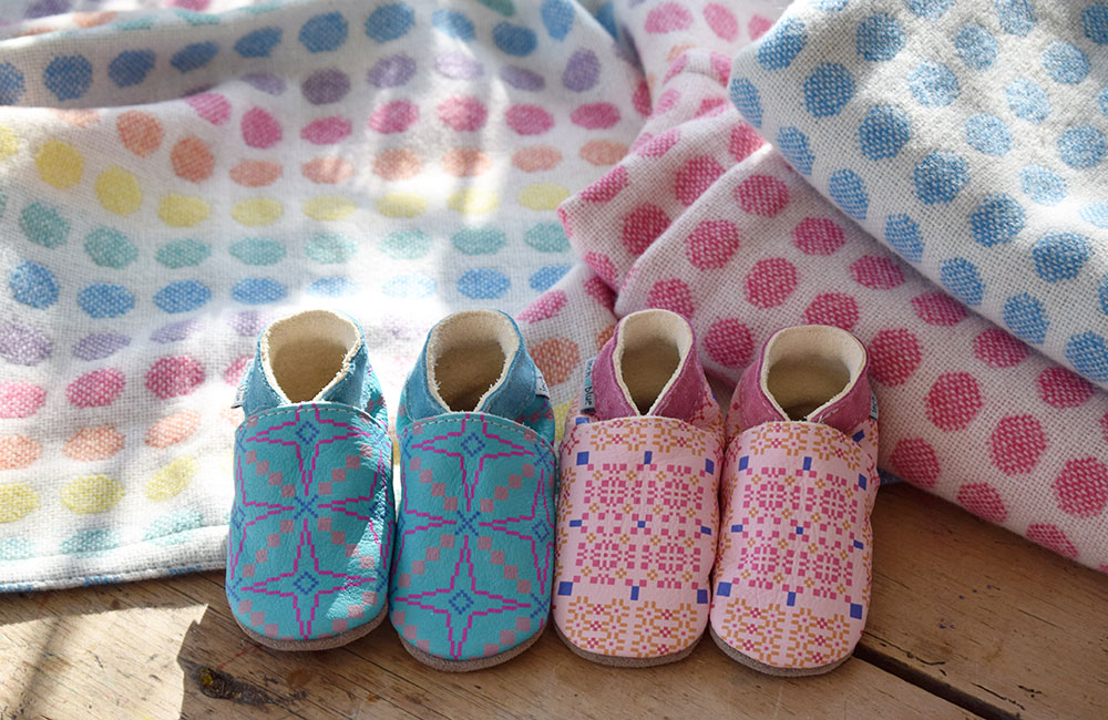 Pair of pink and blue Inch Blue toddlers shoes next to colourful baby blankets