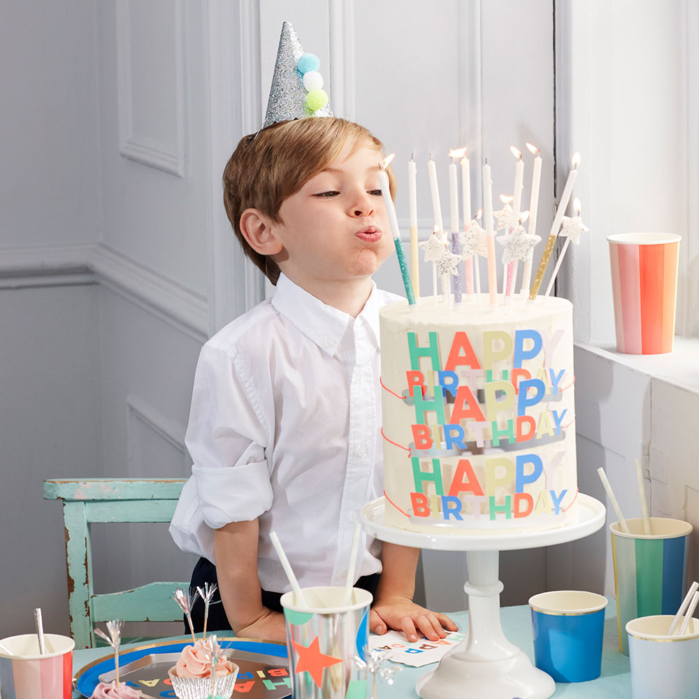 Young boy wearing a party hat, blowing out candle on a large cake