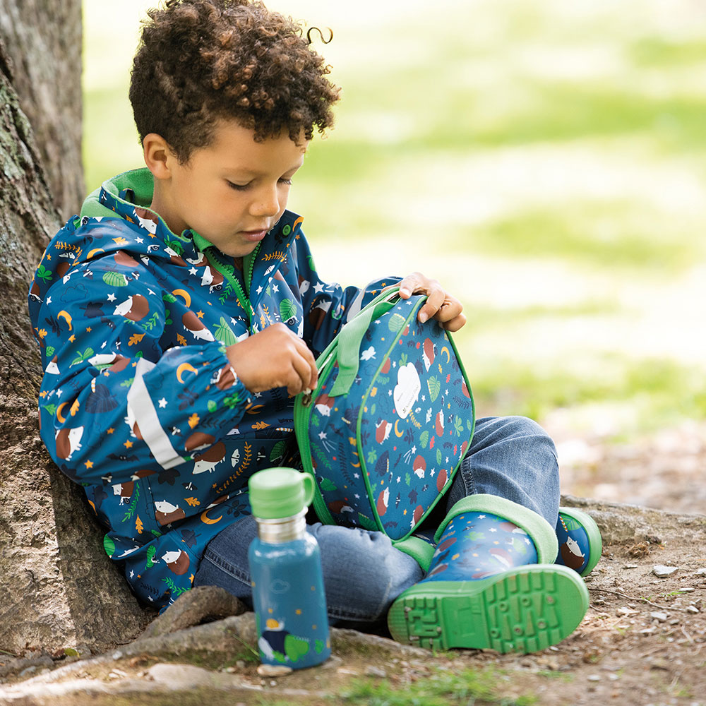 Boy sat against tree in Frugi raincoat with forest print