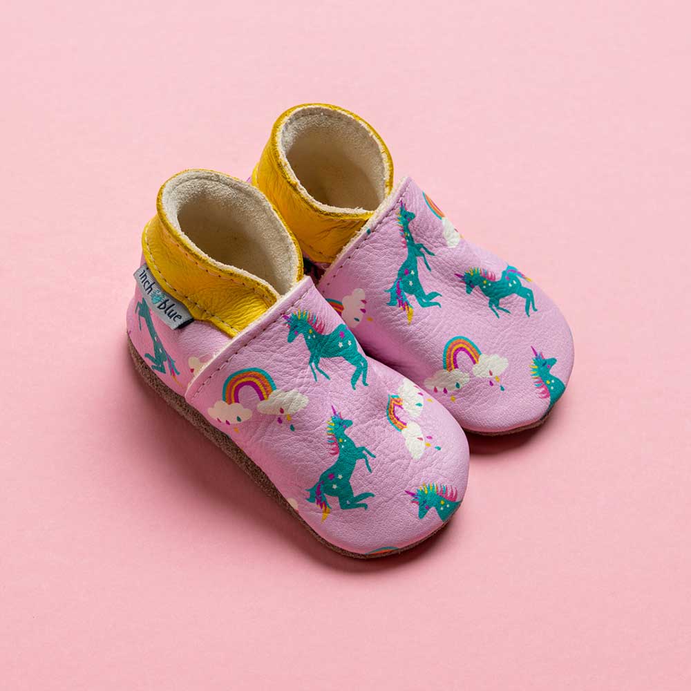A pair of pink handmade leather baby shoes with a unicorn pattern