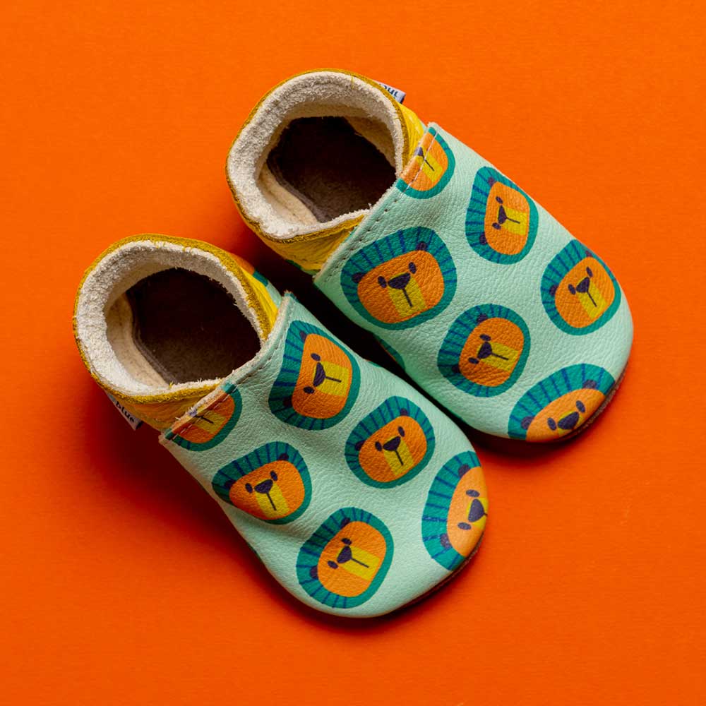 A pair of handmade leather baby shoes with a lions head pattern