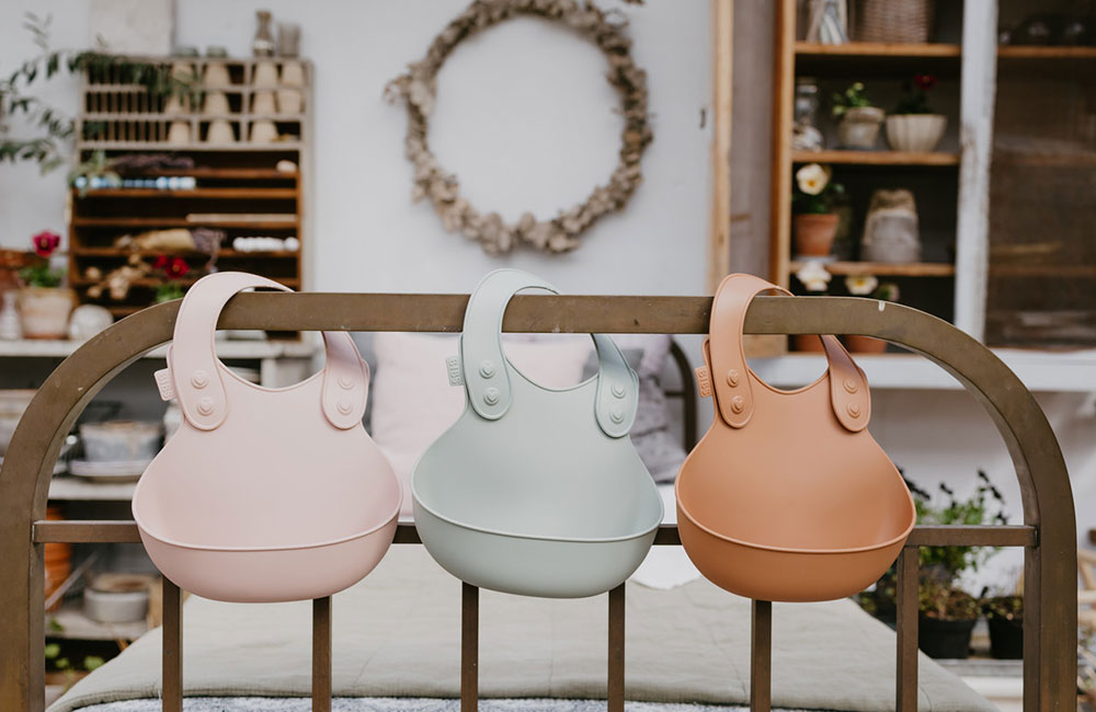 Three pastel coloured childrens bibs hand over a wooden rail