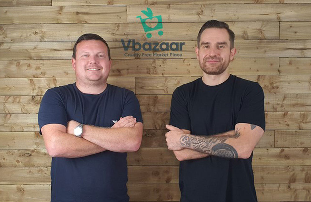 Two men with arms folded stood in front of VBazaar sign