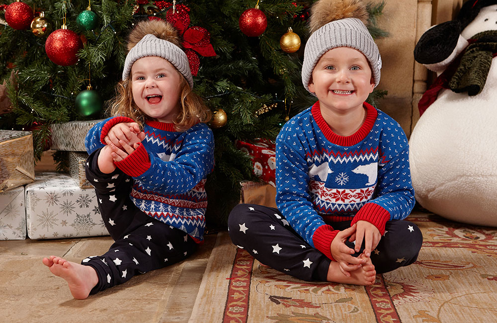 young boy and girl in matching christmas jumpers sat in front of christmas tree